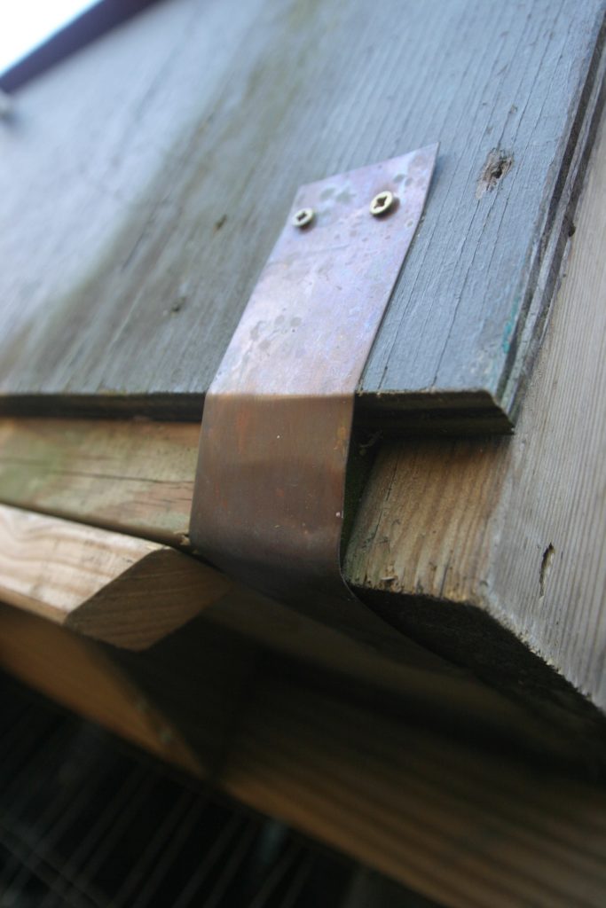 Close-up of flat piece of metal screwed to wood 