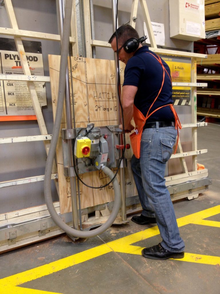 man in bluejeans standing in workshop cutting plywood