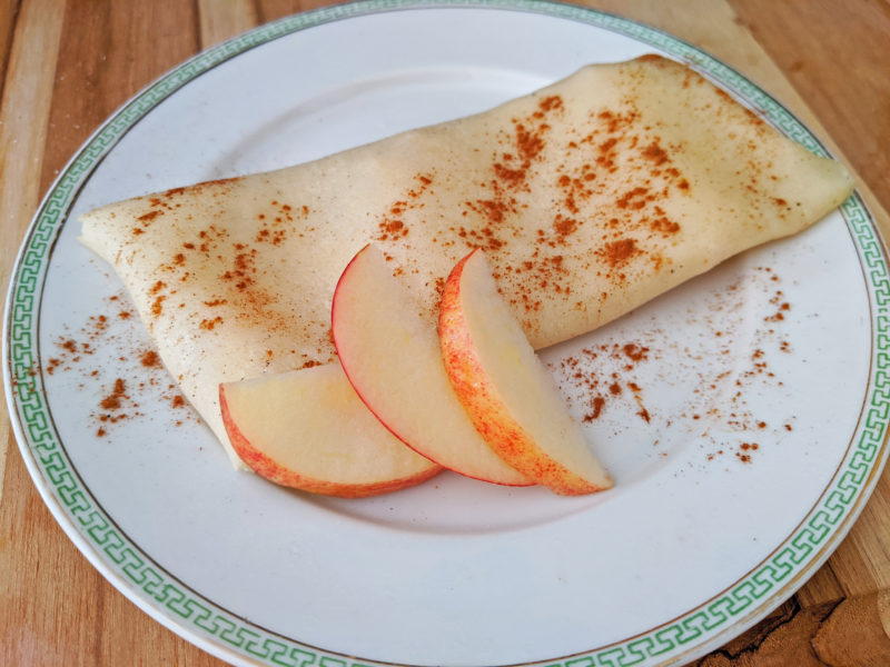quail egg crepes folded on white plate with three apple slices and cinnamon sprinkles