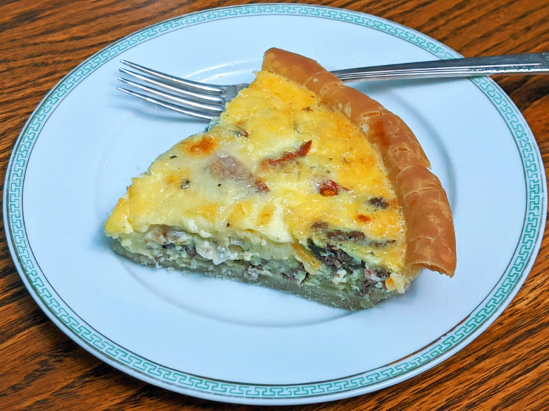 pie-slice of baked quiche on white plate with silver fork
